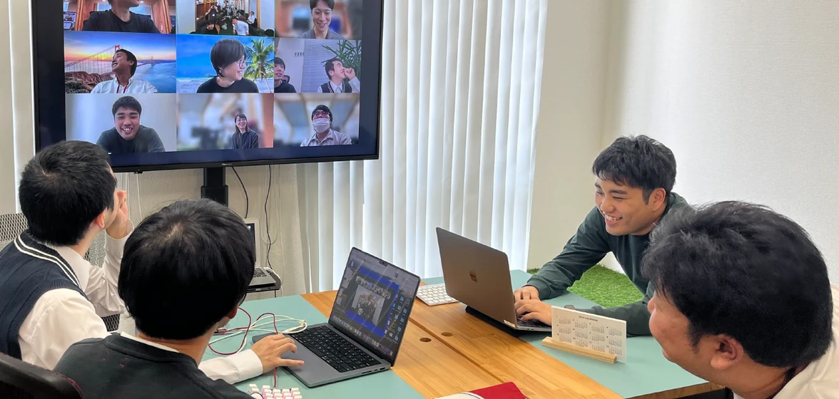 モニター越しにリモートのメンバーとつなぎ、会議室で打ち合わせをする社員